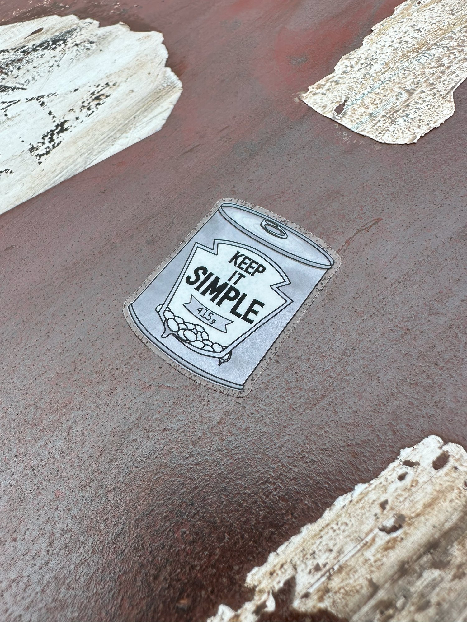 A Keep It Simple heuristic sticker among peeling stickers on red metal